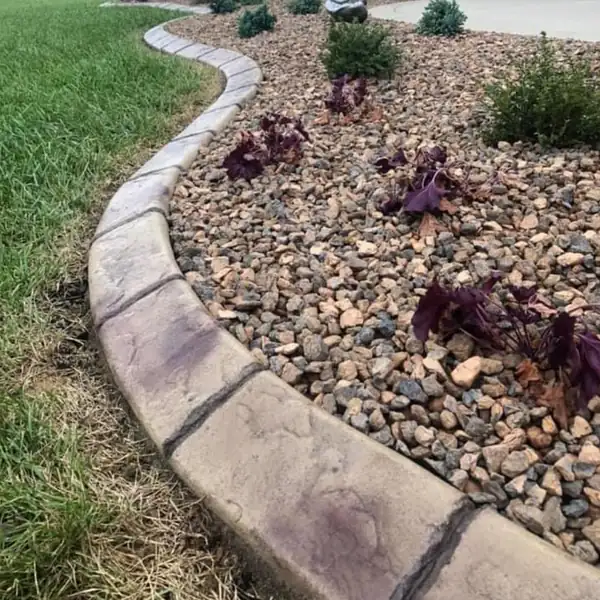 Curved stamped concrete curb edging a river rock flower bed next to the lawn