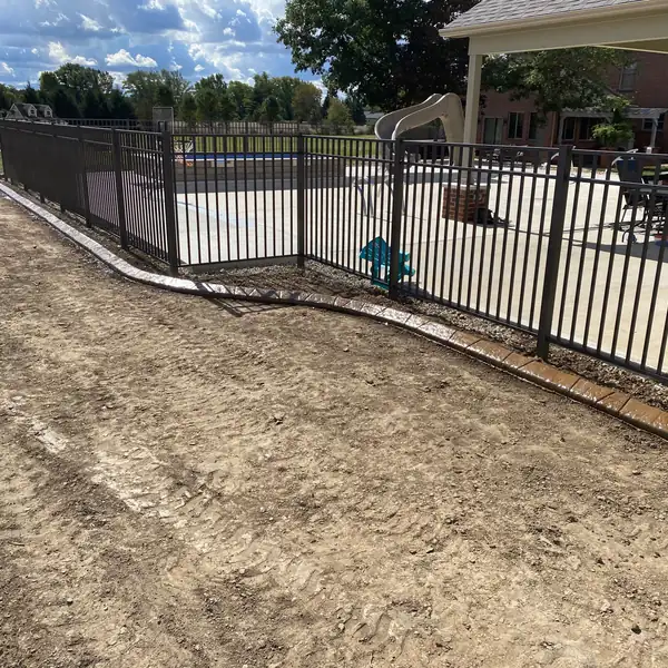 New concrete curb running along a black fence beside a pool patio