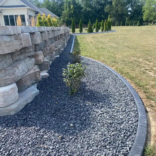 Concrete curb along a black rock bed at the base of a stone wall
