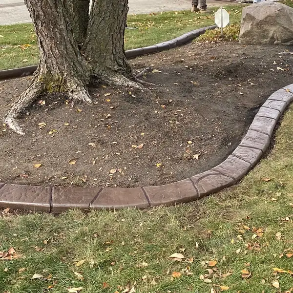 Wide view of a concrete curb around a tree bed in a lawn